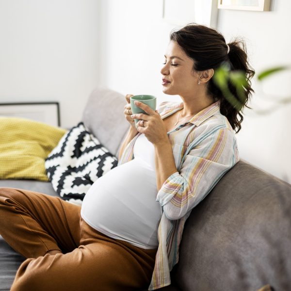 Schwangere sitzt auf dem Sofa und genießt eine Tasse Tee