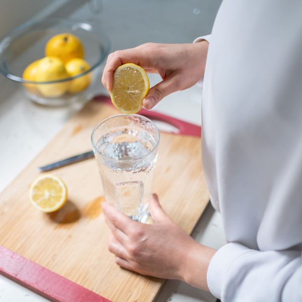 Person presst Zitronensaft in Wasserglas